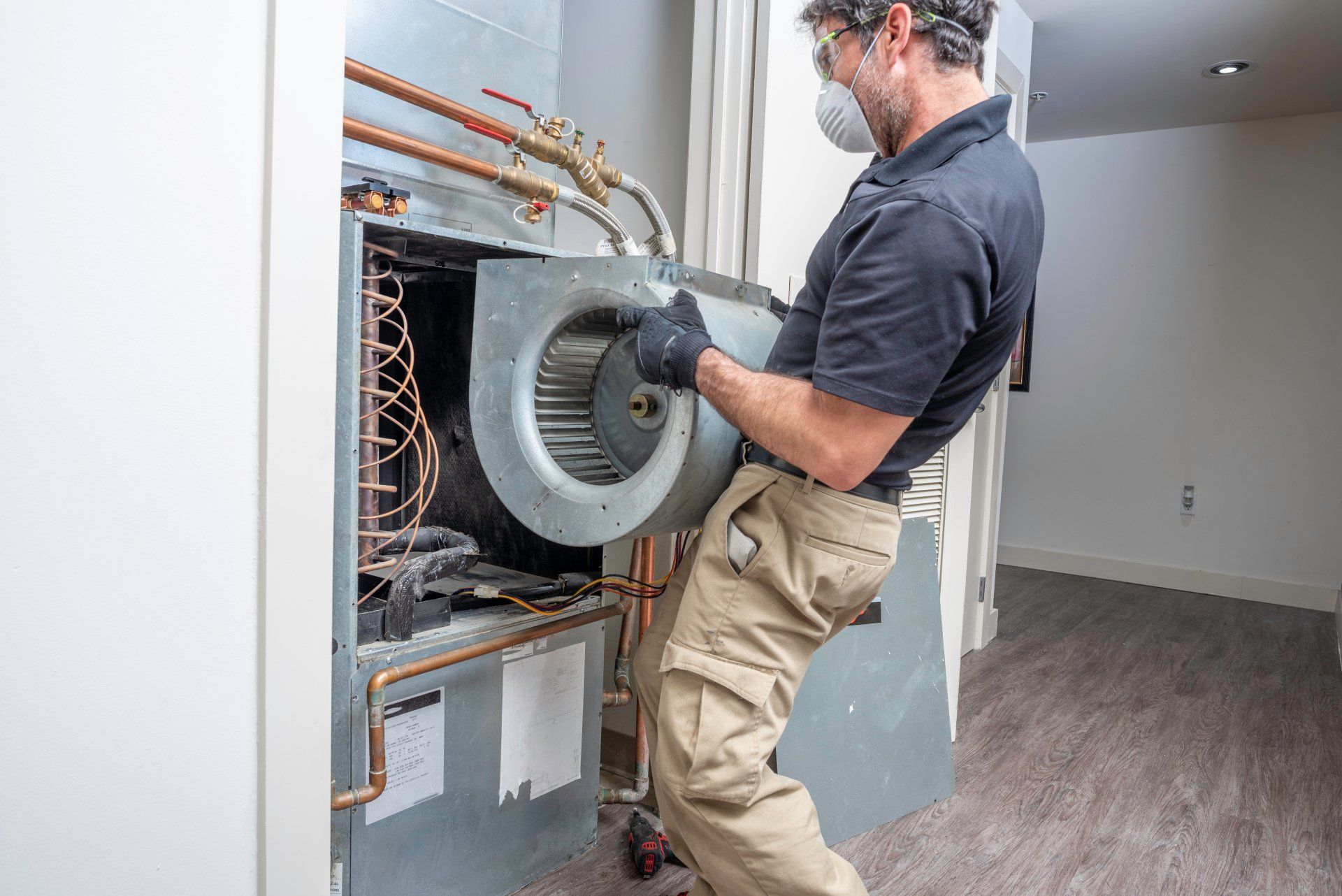 HVAC contractor wearing a mask and safety glasses repairing a motor on a heat pump