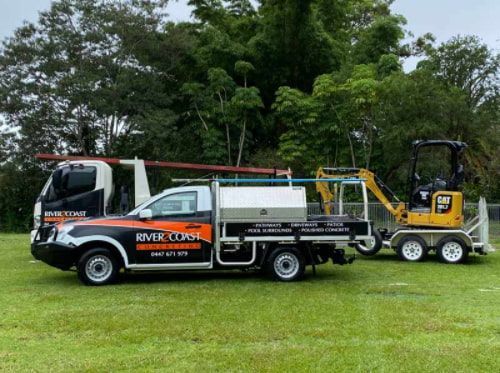 A Truck With A Trailer Attached To It Is Parked In A Grassy Field  — River2Coast Concreting in Boambee, NSW