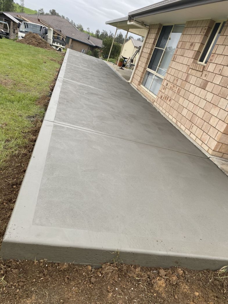 A Concrete Walkway Is Being Built In Front Of A Brick House  — River2Coast Concreting in Boambee, NSW