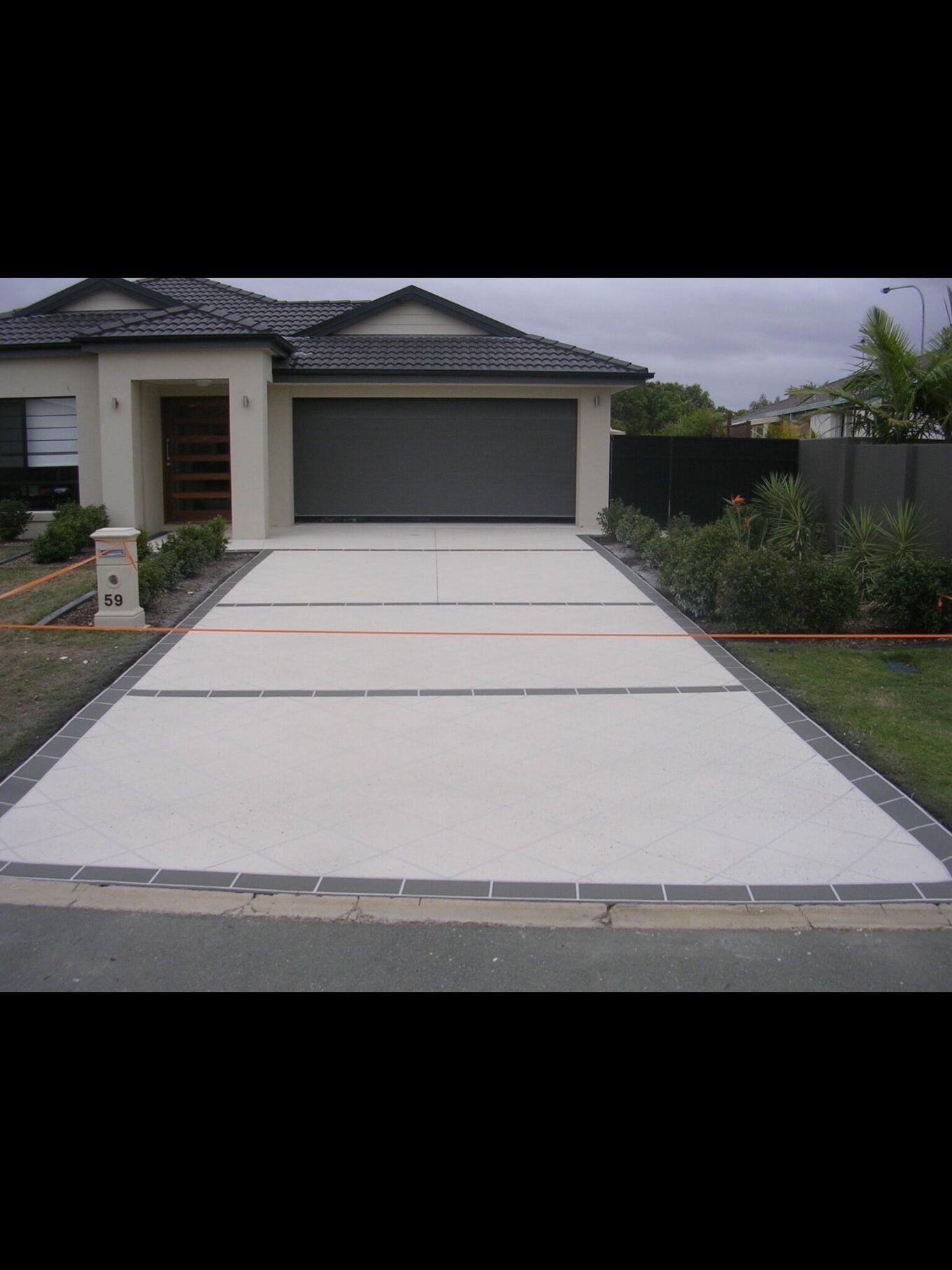 A Driveway Leading To A House With A Garage Door  — River2Coast Concreting in Boambee, NSW