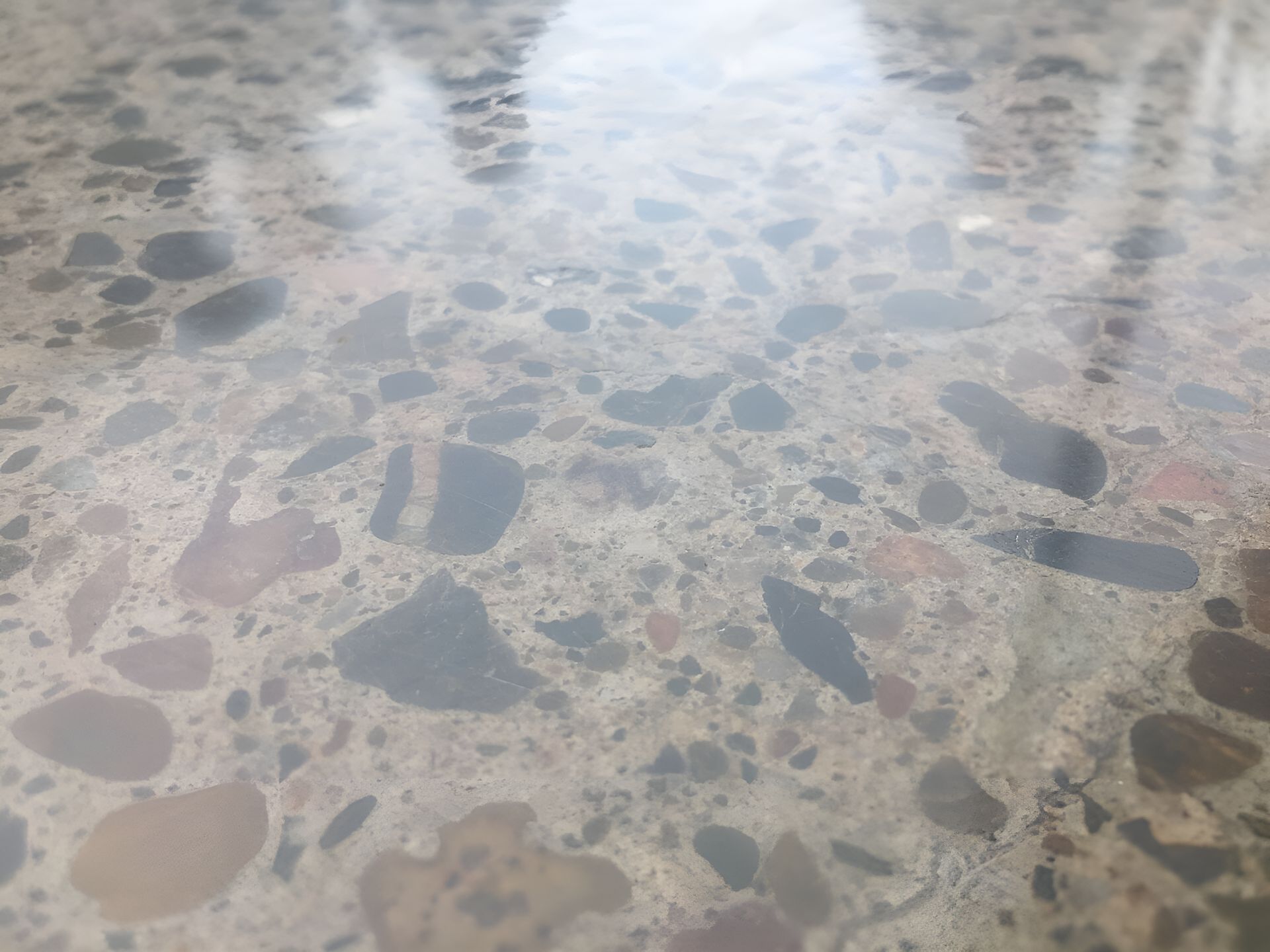 A Close Up Of A Shiny Concrete Floor With A Lot Of Rocks On It  — River2Coast Concreting in Boambee, NSW