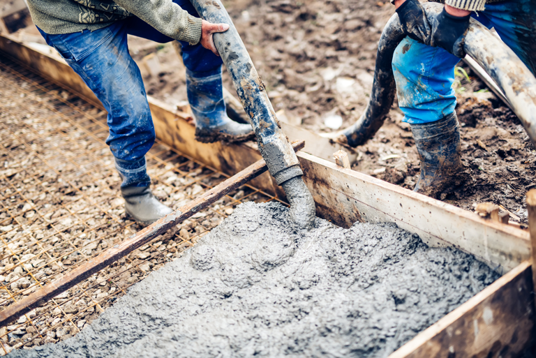A Couple Of Men Are Pouring Concrete Into A Hole In The Ground  — River2Coast Concreting in Boambee, NSW