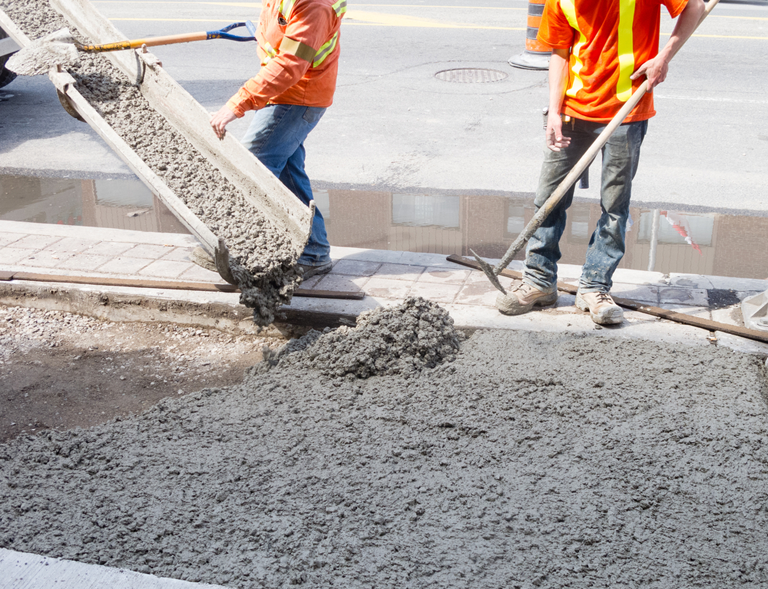 Two Construction Workers Are Pouring Concrete On A Sidewalk  — River2Coast Concreting in Boambee, NSW