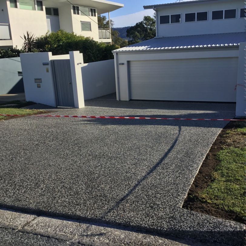 A Driveway Leading To A House With A White Garage Door  — River2Coast Concreting in Boambee, NSW