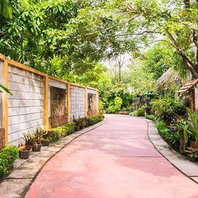 A Red Concrete Path Leading To A House Surrounded By Trees And Bushes  — River2Coast Concreting in Grafton, NSW