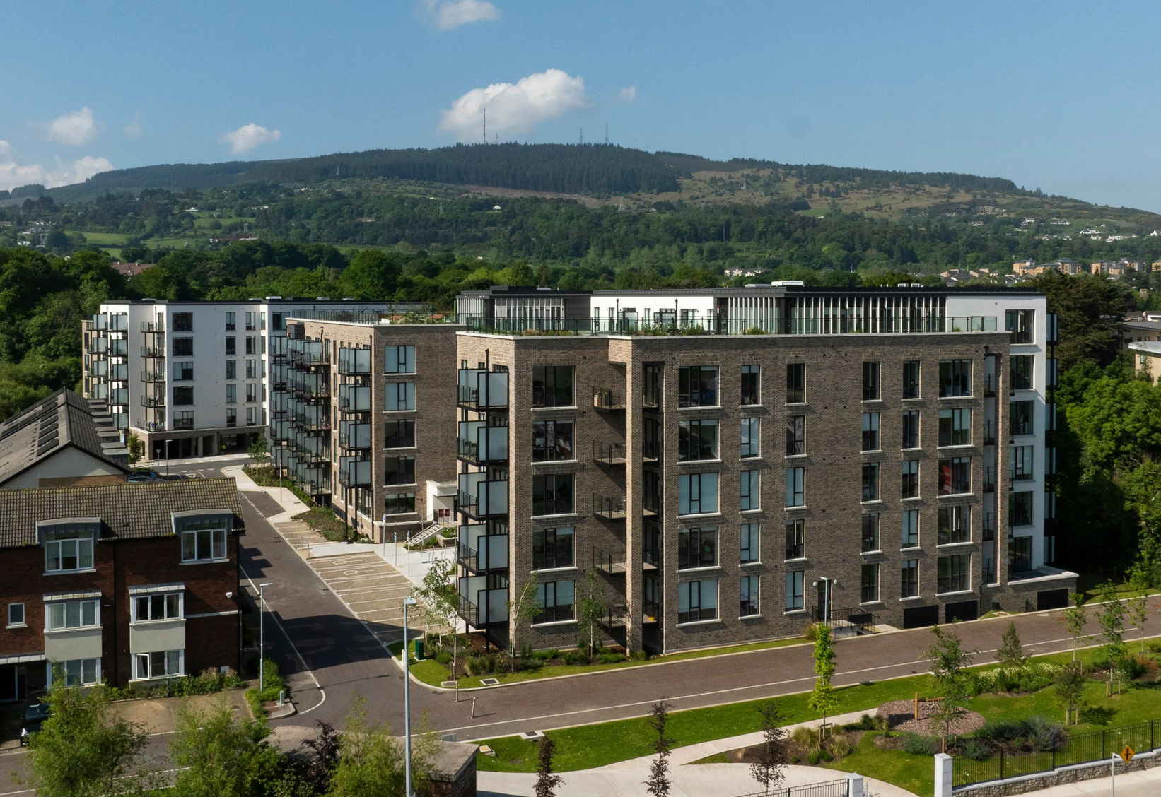 Modern apartment buildings with balconies on a hillside under a partly cloudy sky