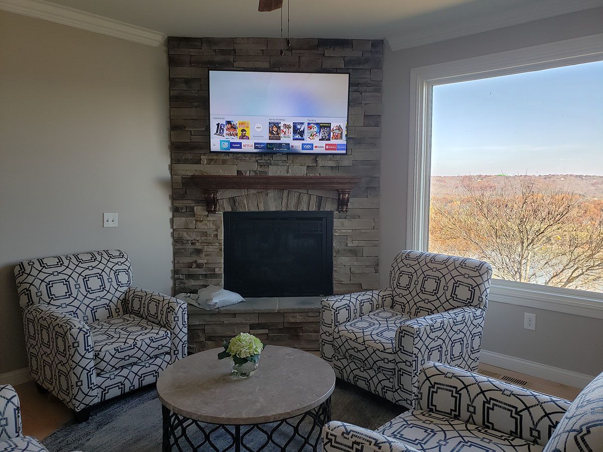 A living room with a fireplace , chairs , a coffee table and a flat screen tv.