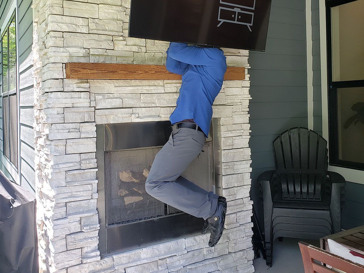 A man is carrying a box over his head while climbing a fireplace.