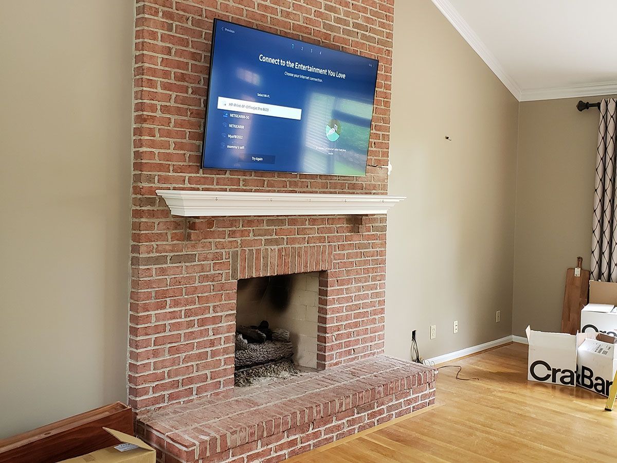 A living room with a brick fireplace and a flat screen tv mounted to the wall.