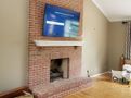 A living room with a brick fireplace and a flat screen tv mounted to the wall.