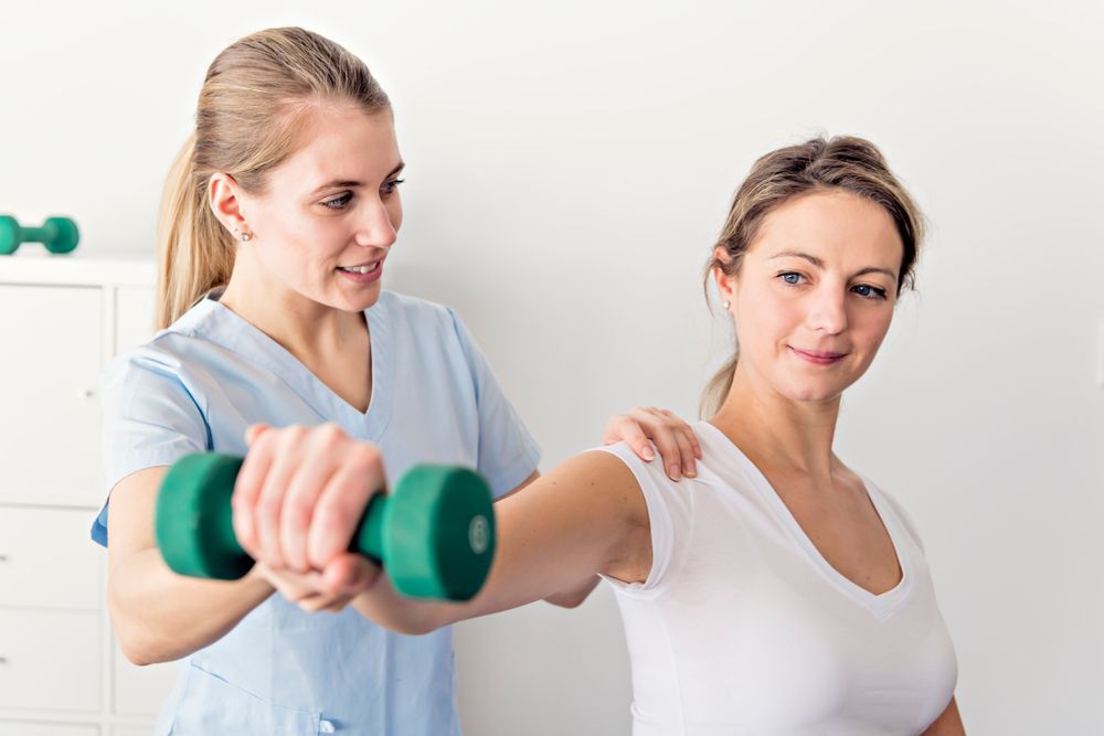 A nurse is helping a woman lift a green dumbbell. — HealthPoint Mingara In Tumbi Umbi, NSW