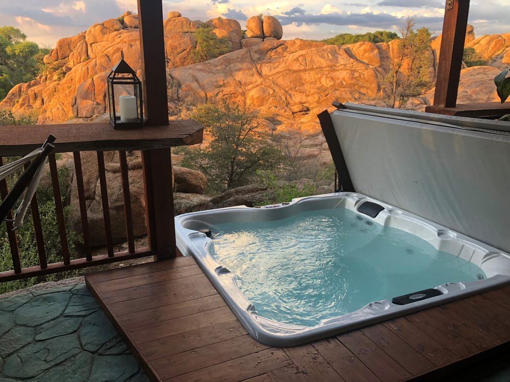 A hot tub on a wooden deck overlooks a rocky landscape at sunset, with a decorative lantern on a nearby railing.
