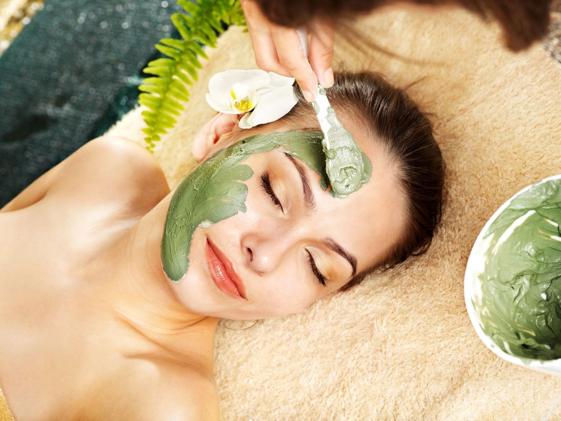 Una donna riceve una maschera facciale verde con un pennello durante un trattamento in una spa.