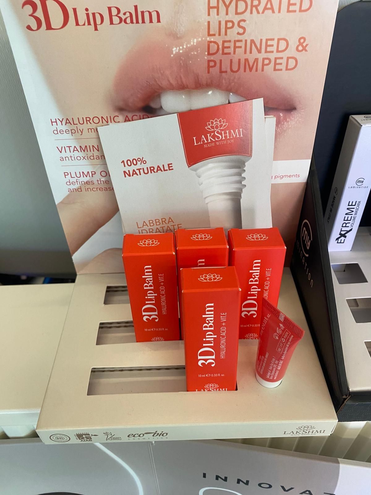 Espositore di tubetti di balsamo labbra 3D in confezione rossa e bianca su uno scaffale di un negozio con la scritta