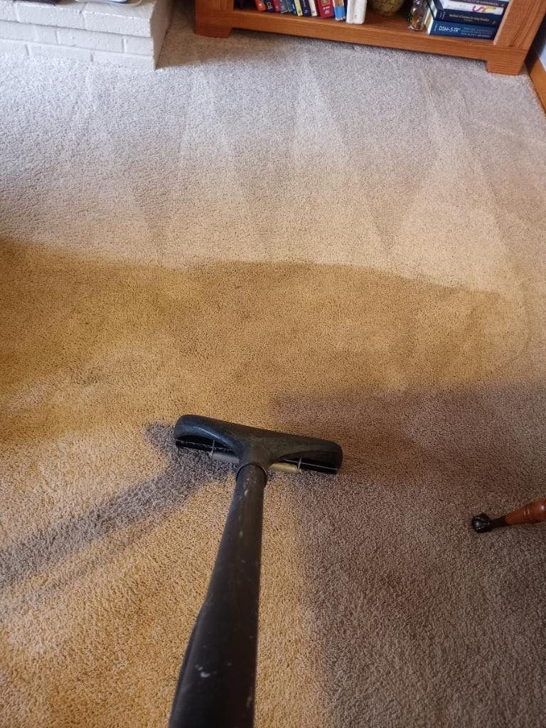 A vacuum cleaner is cleaning a carpet in a living room.