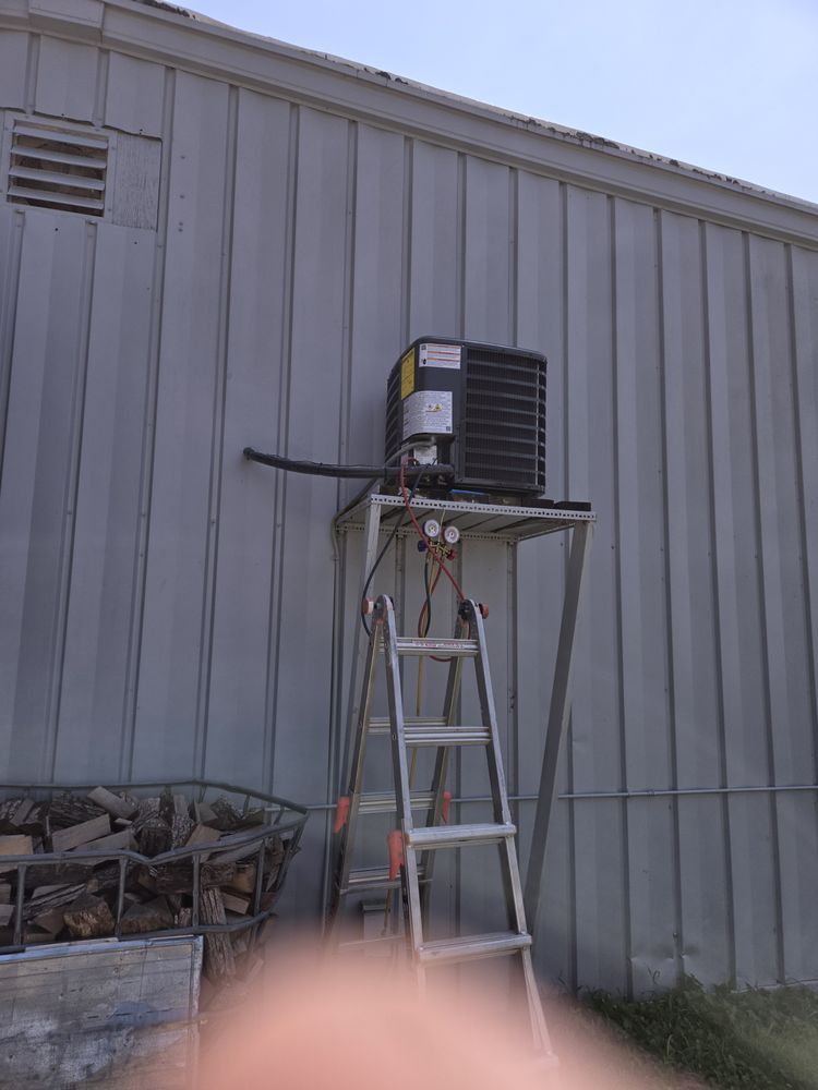 Air conditioner unit on a metal stand outside a metal building, with a ladder leaning against the stand.