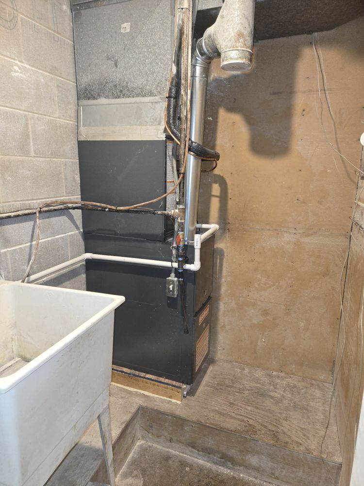 Basement with furnace, utility sink, and concrete walls. Black furnace on a concrete floor.