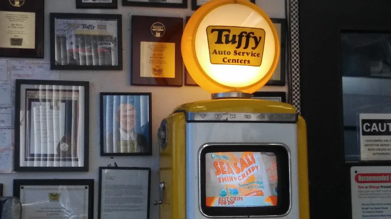 Vintage Tuffy Auto Service sign with illuminated logo on a yellow fuel pump. Interior wall with framed documents.