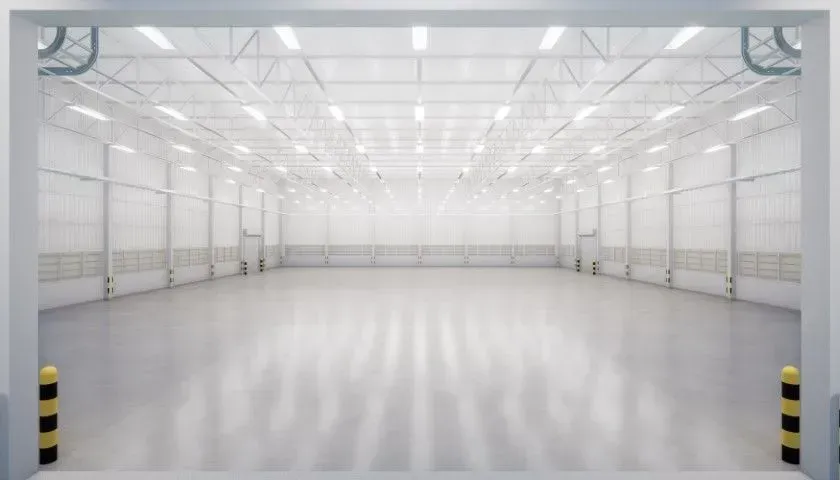 Empty white industrial warehouse interior with bright lights and reflective floor
