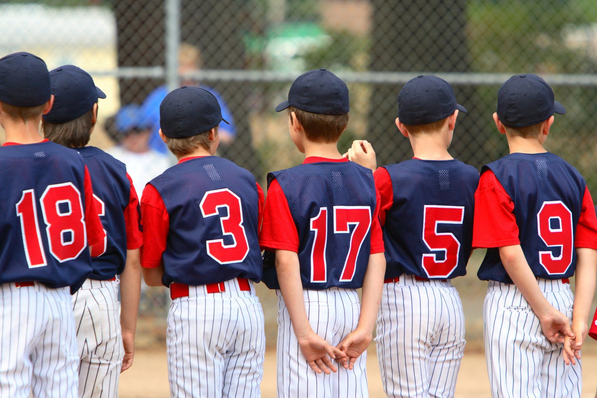 Youth baseball players in uniforms, backs to the camera, standing in a line, numbers on jerseys.