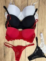 Sujetadores y tanga en blanco, negro y rojo, dispuestos sobre madera.