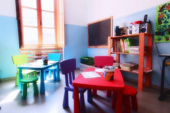 aula scuola per l'infanzia con lavagna sul muro e banchi e sedie di diverso colore