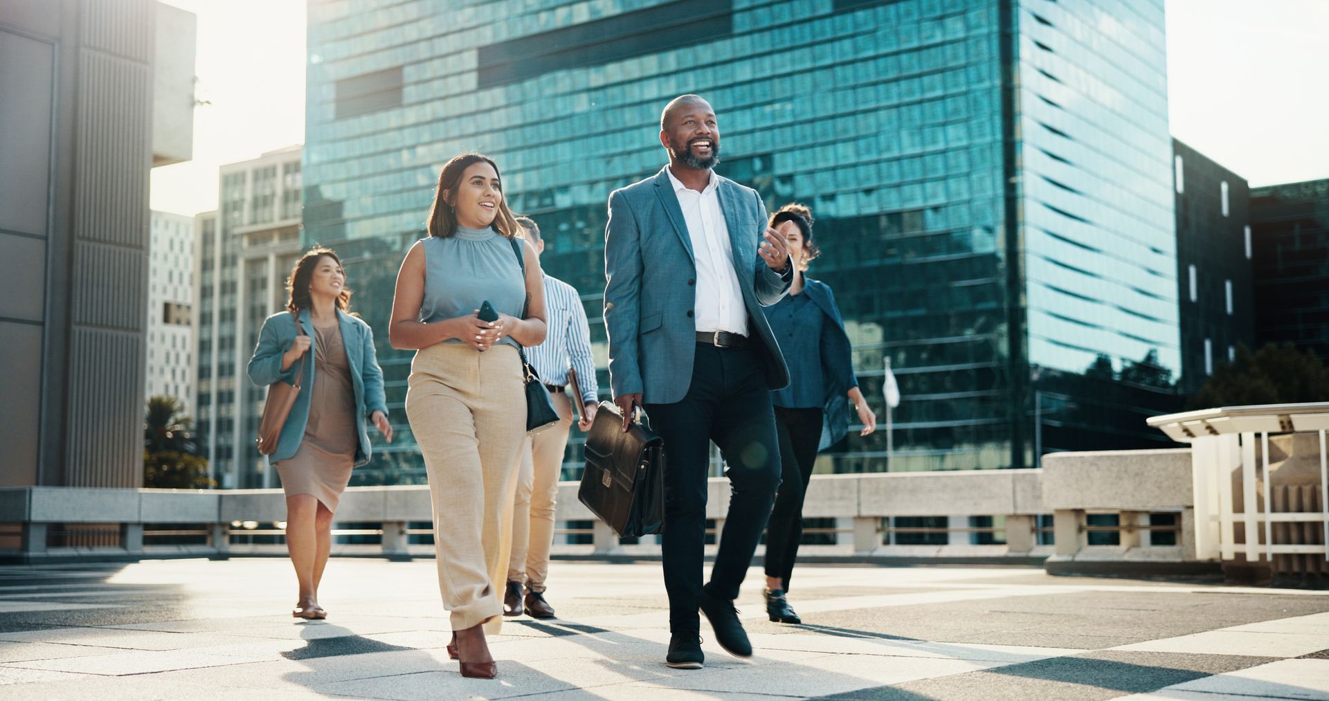 Group of people walking outside a modern building, smiling and looking ahead.