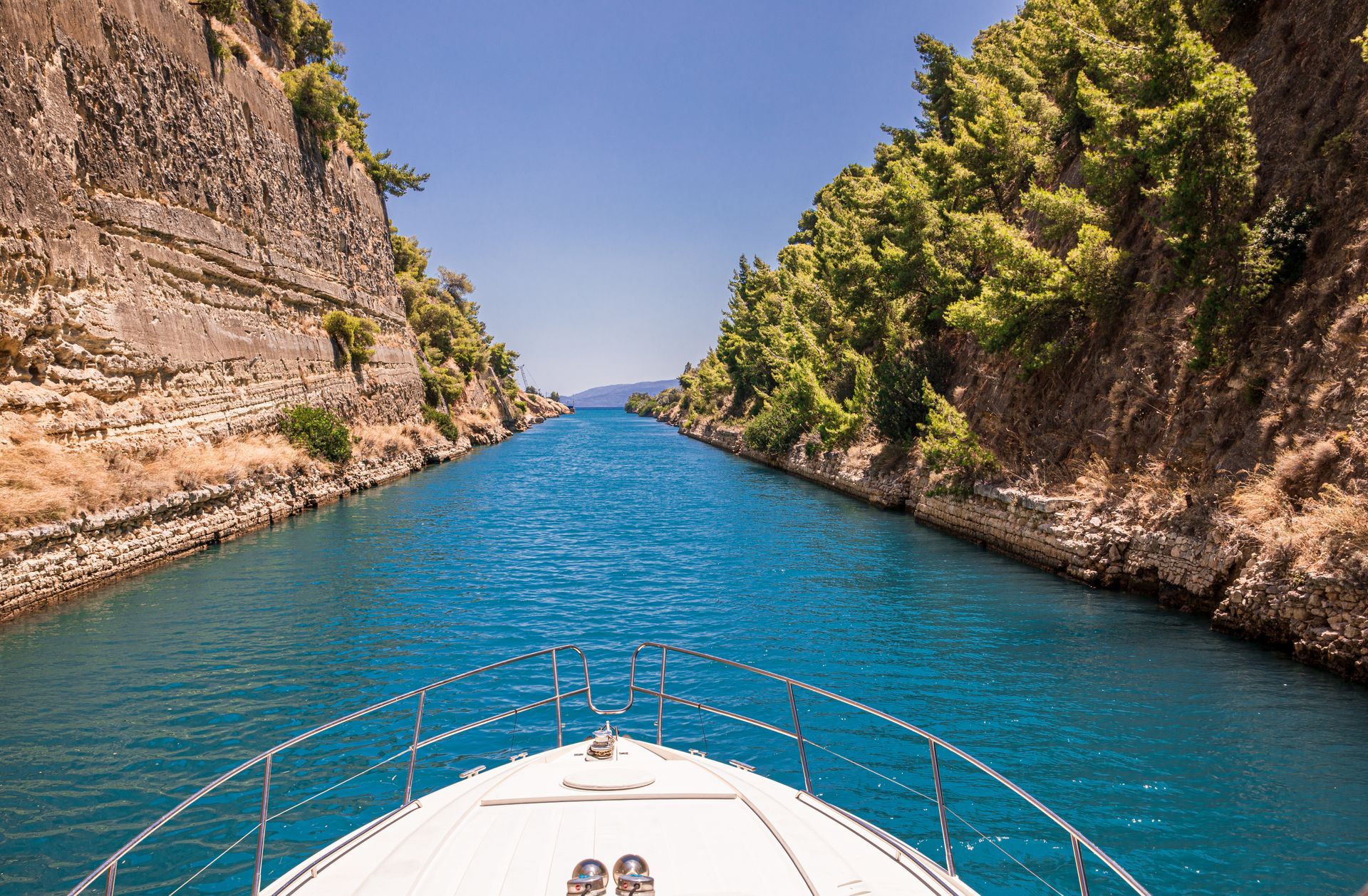 Boat navigating the Corinth Canal, Greece. Emerald water, steep rock walls, blue sky.