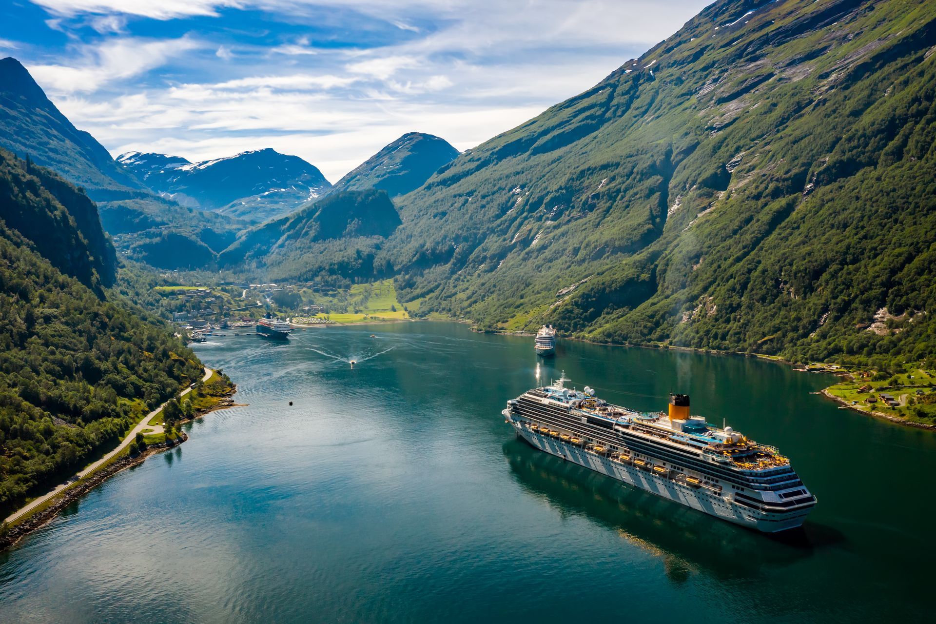 Cruise ship in a fjord surrounded by green mountains and blue water.