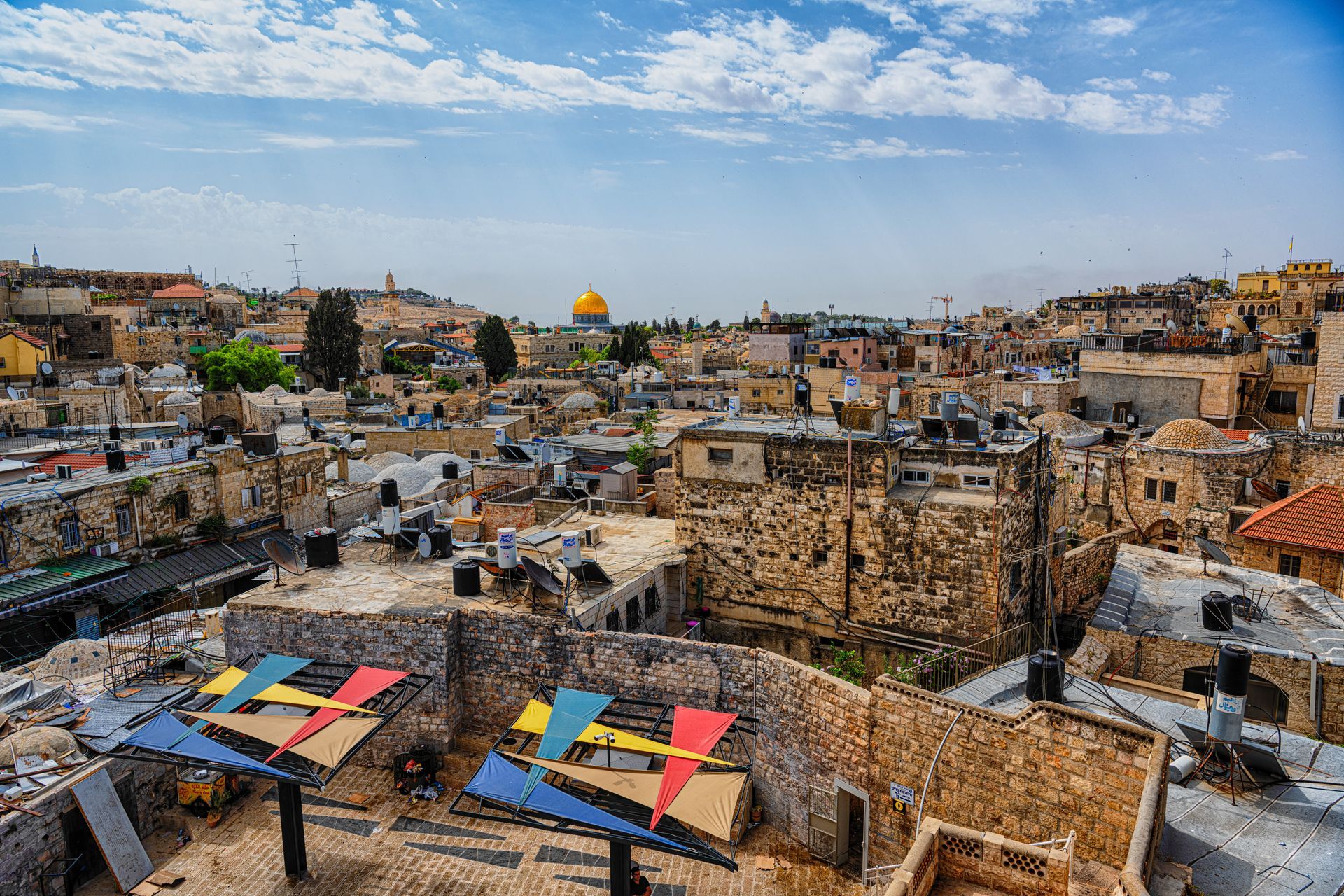Jerusalem cityscape with the golden Dome of the Rock, featuring colorful geometric art on a rooftop.