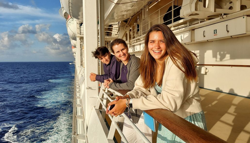 Three people smiling on a cruise ship deck, looking at the ocean.