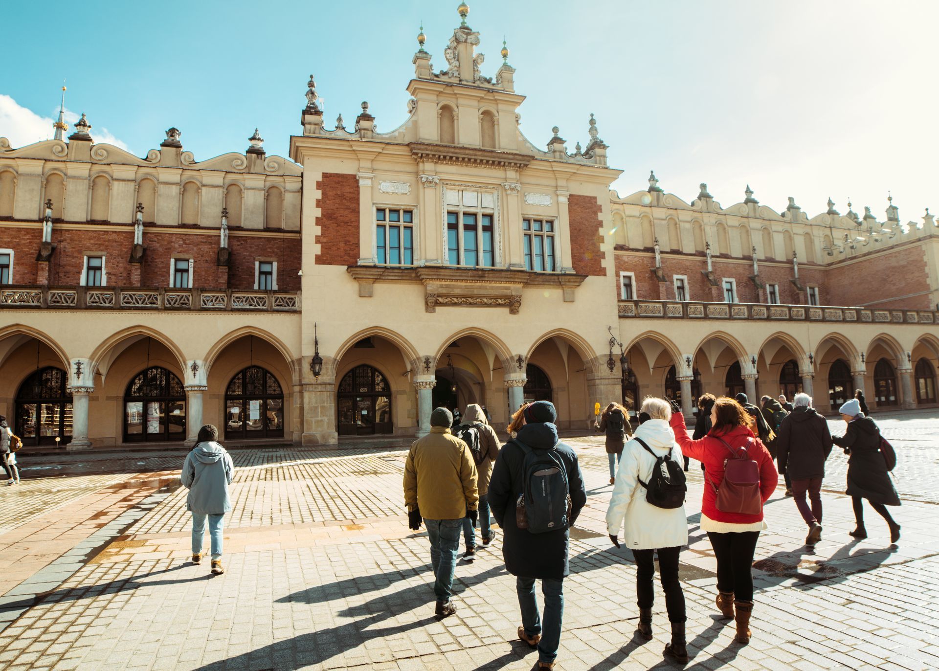 People walk toward Cloth Hall, Krakow, Poland. Arched building facade, sunny day.