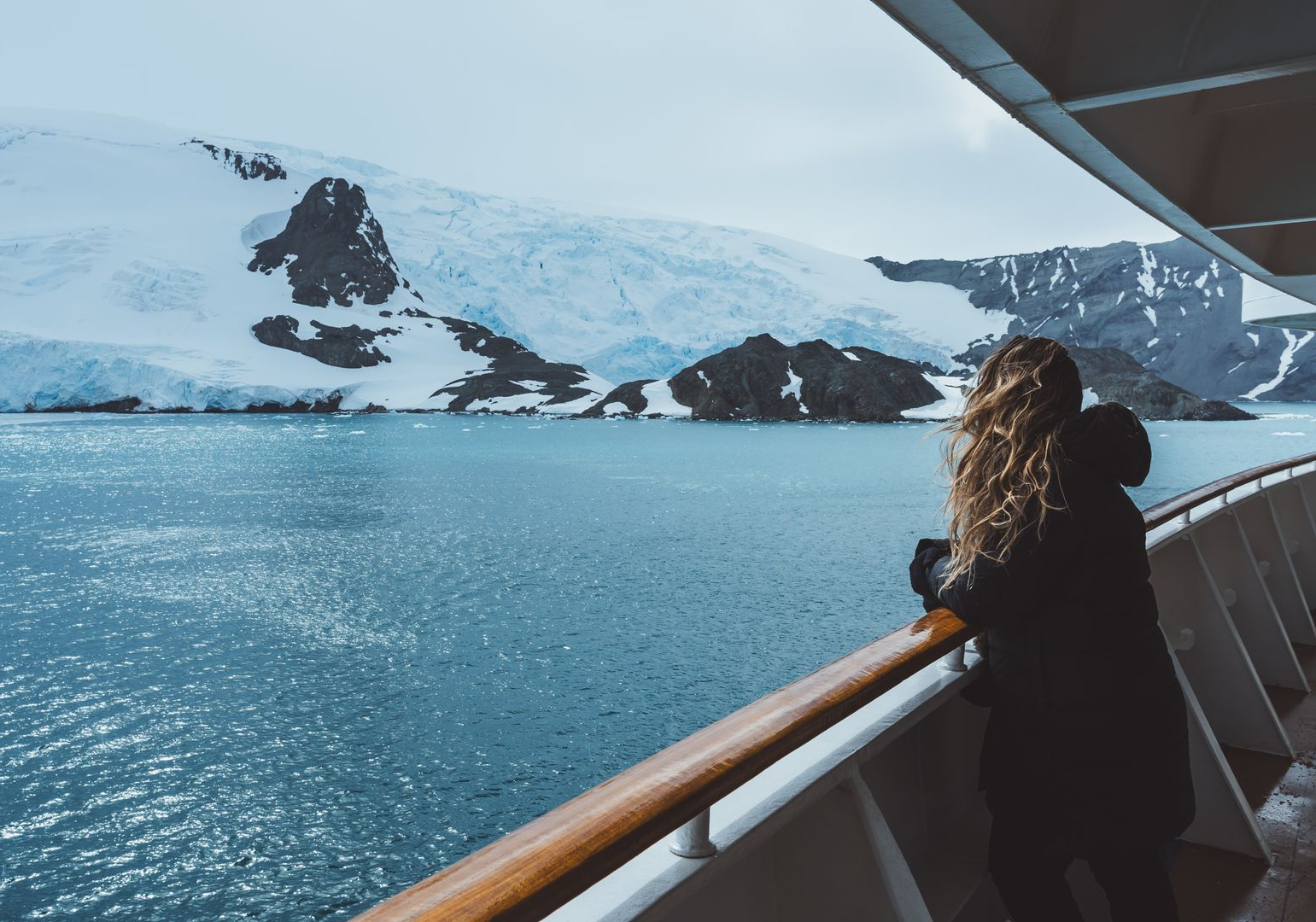 Boats docked in a harbor, with a bridge, marshland, and waterway in the background under a sunny sky.
