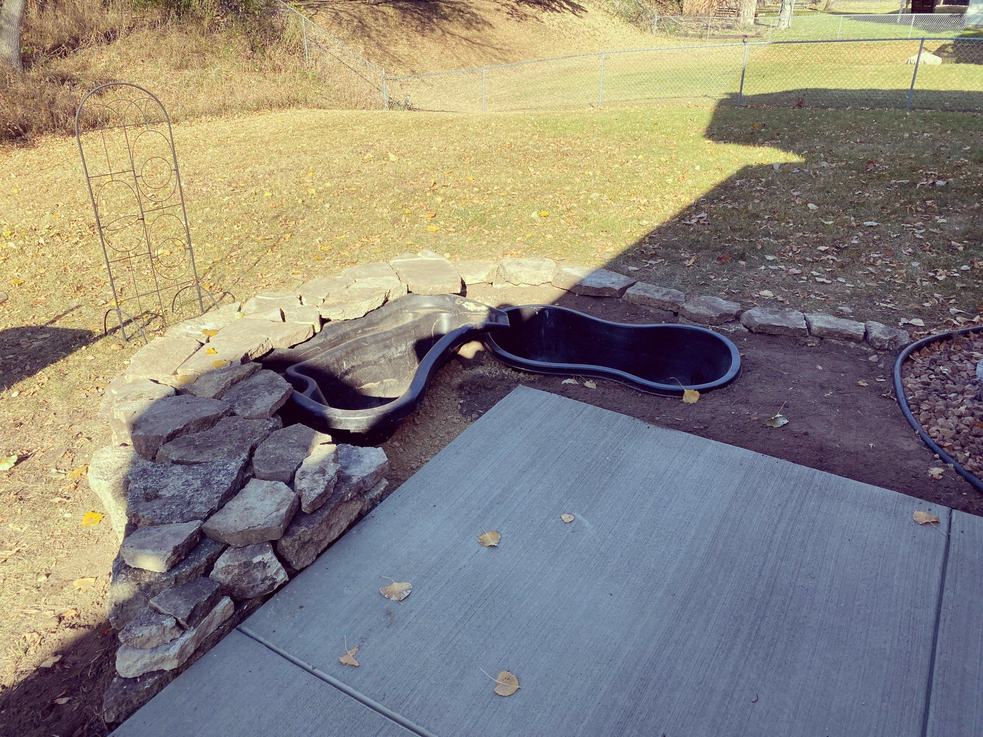 A black snake is laying on the ground next to a pond.