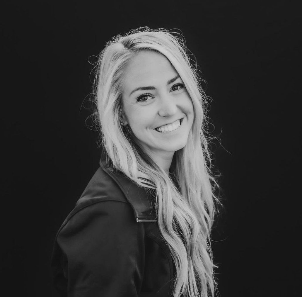 A woman with long blonde hair is smiling in a black and white photo.