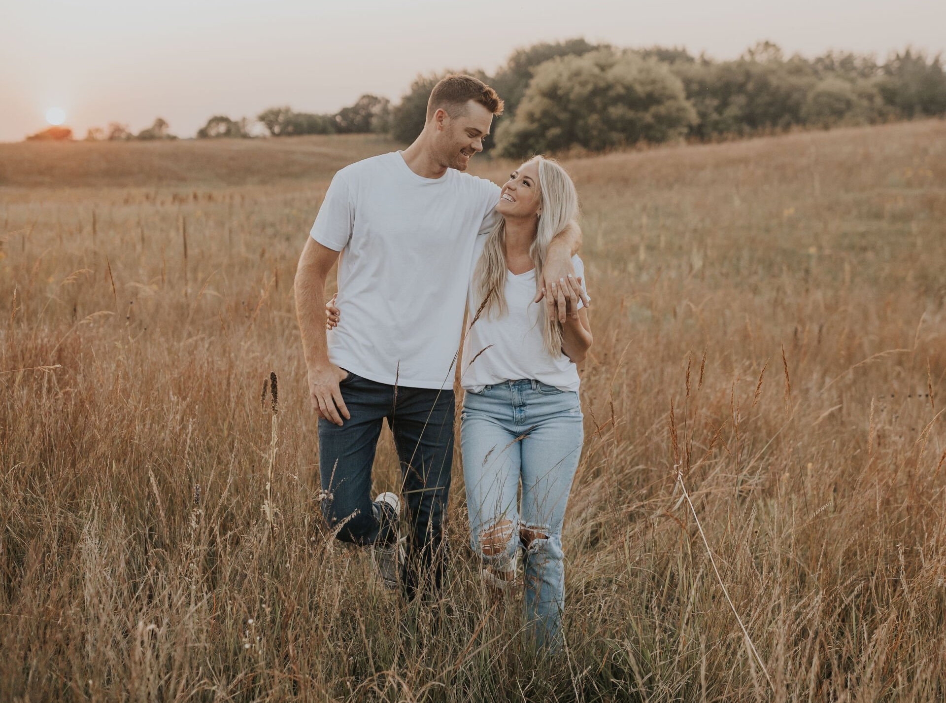 A man and a woman are walking through a field of tall grass.
