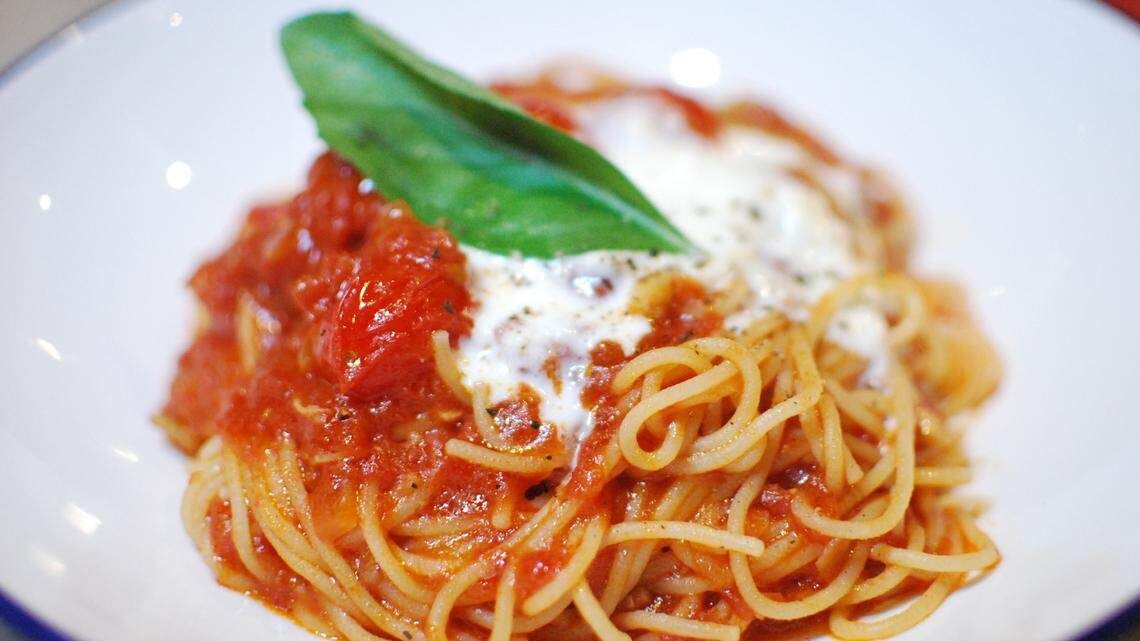 Spaghetti dish with red sauce, cheese, and basil leaf on a white plate.