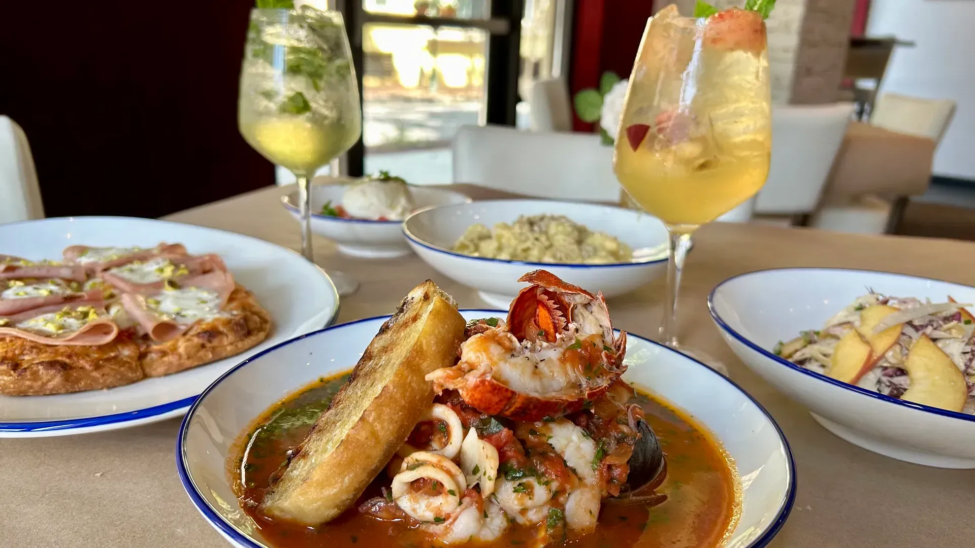 A table with seafood dishes, cocktails, and a flatbread in a restaurant setting.