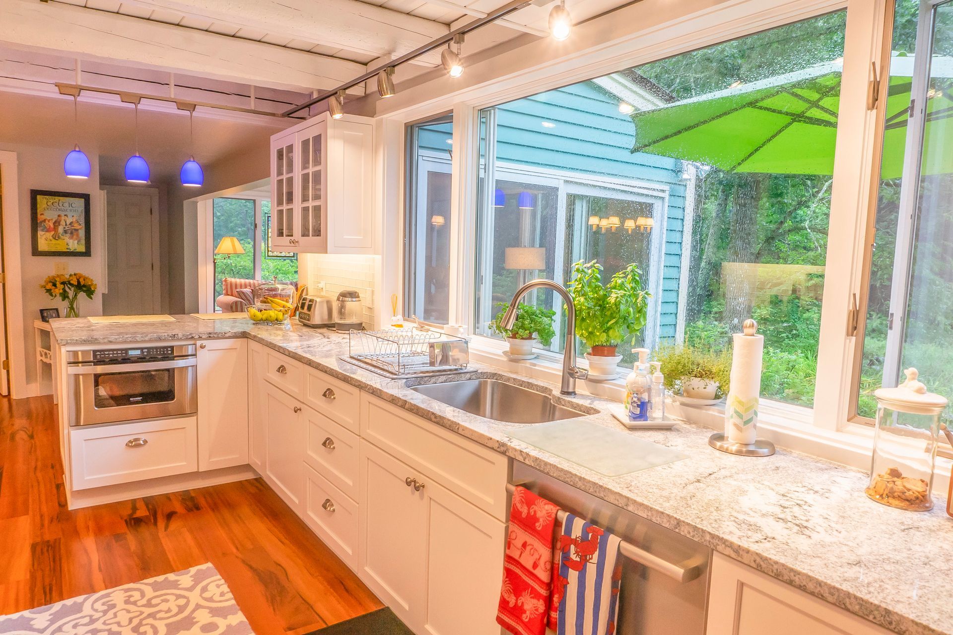 A kitchen with white cabinets , granite counter tops , a sink and a large window.