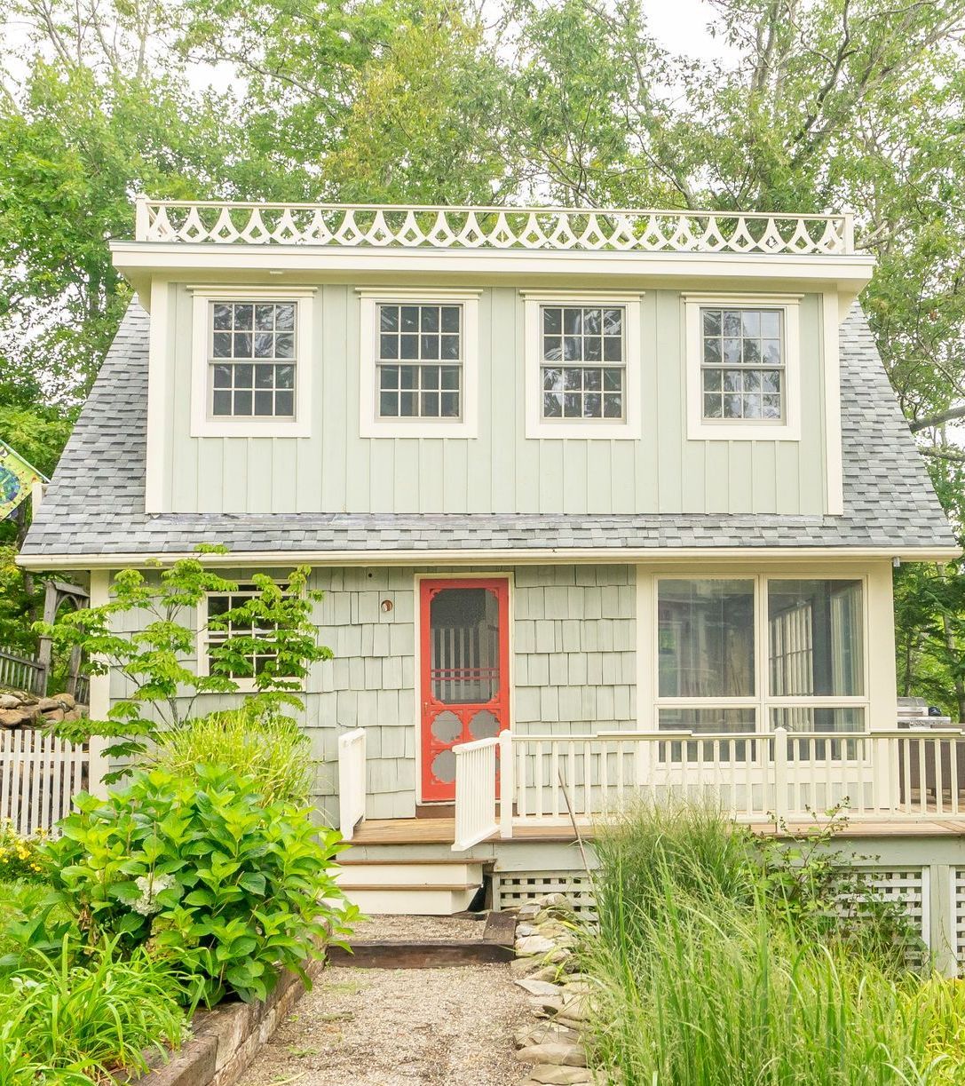 Light green cottage with red door, white trim, small deck, and decorative roof.