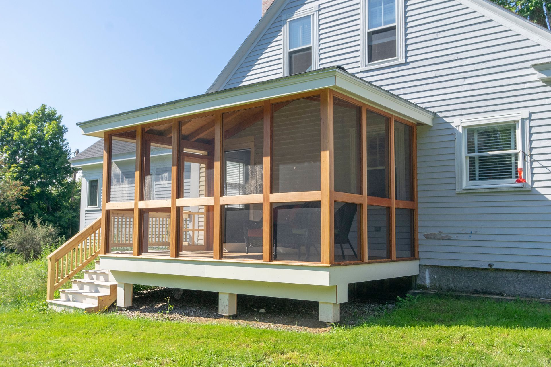 A screened in porch with stairs is in the backyard of a house.