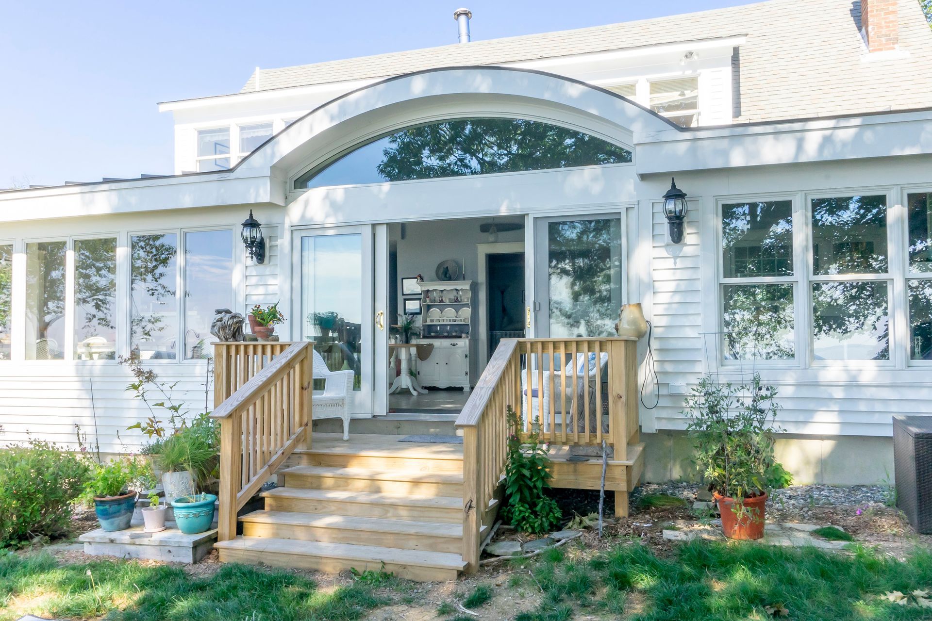 A remodeled coastal home with a white exterior, large arched window, and sliding glass doors leading