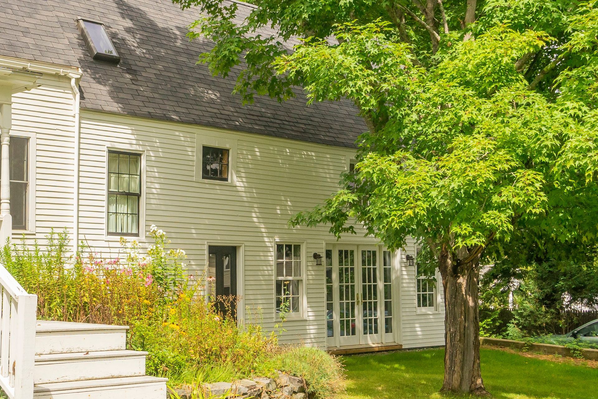 A white house with a black roof and a tree in front of it.