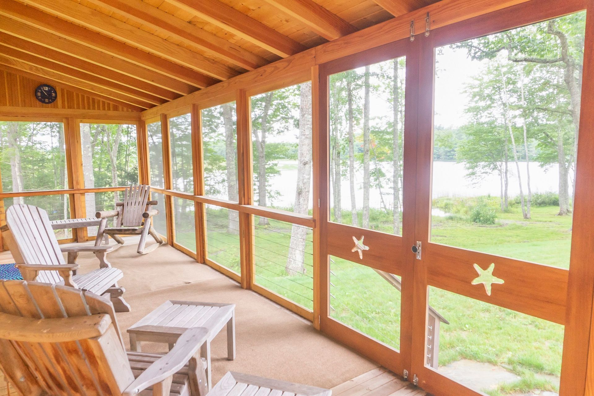 A screened in porch with chairs and a table and a view of a lake.