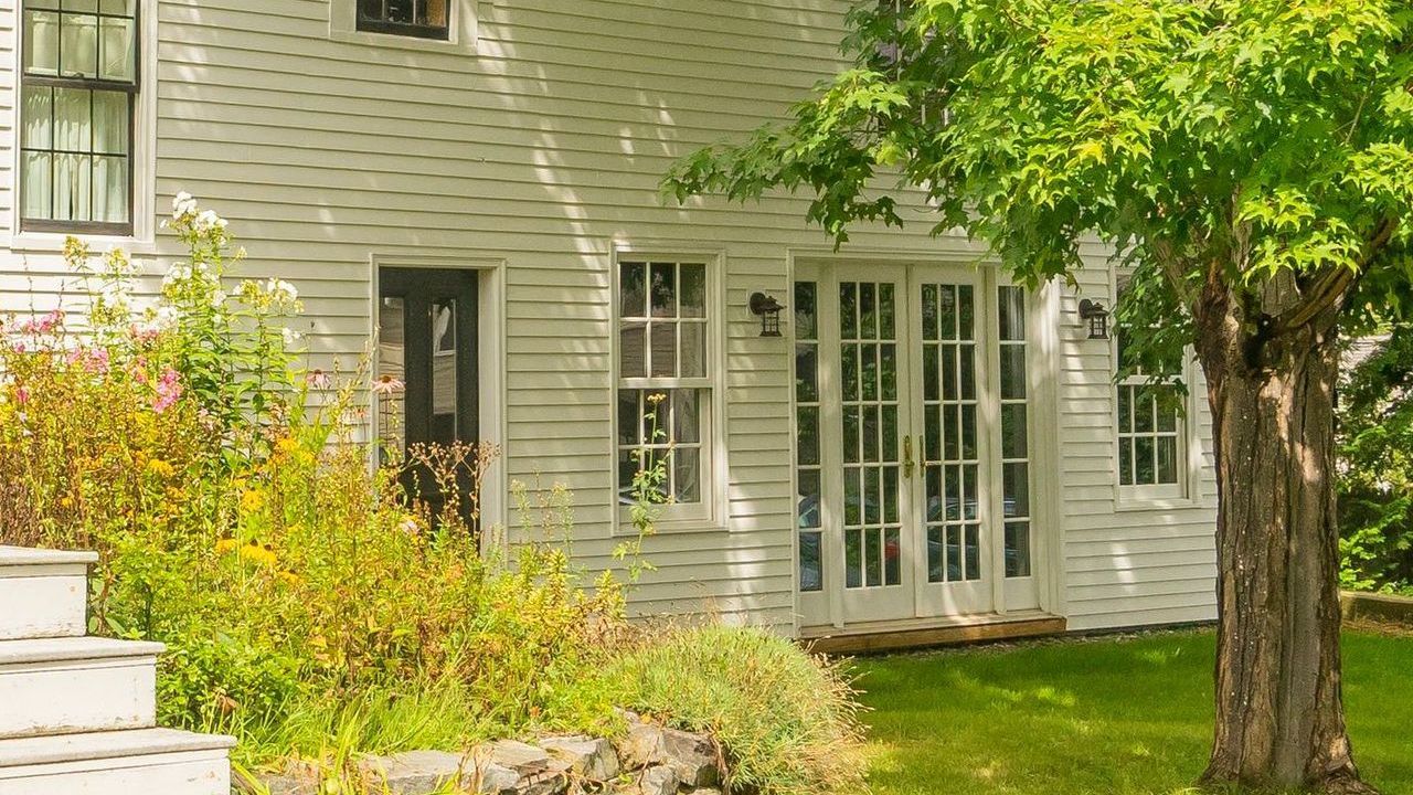 Whitecap Builders' home in Belfast, Maine, with white siding, French doors, a garden, and a large tree on a finished site.