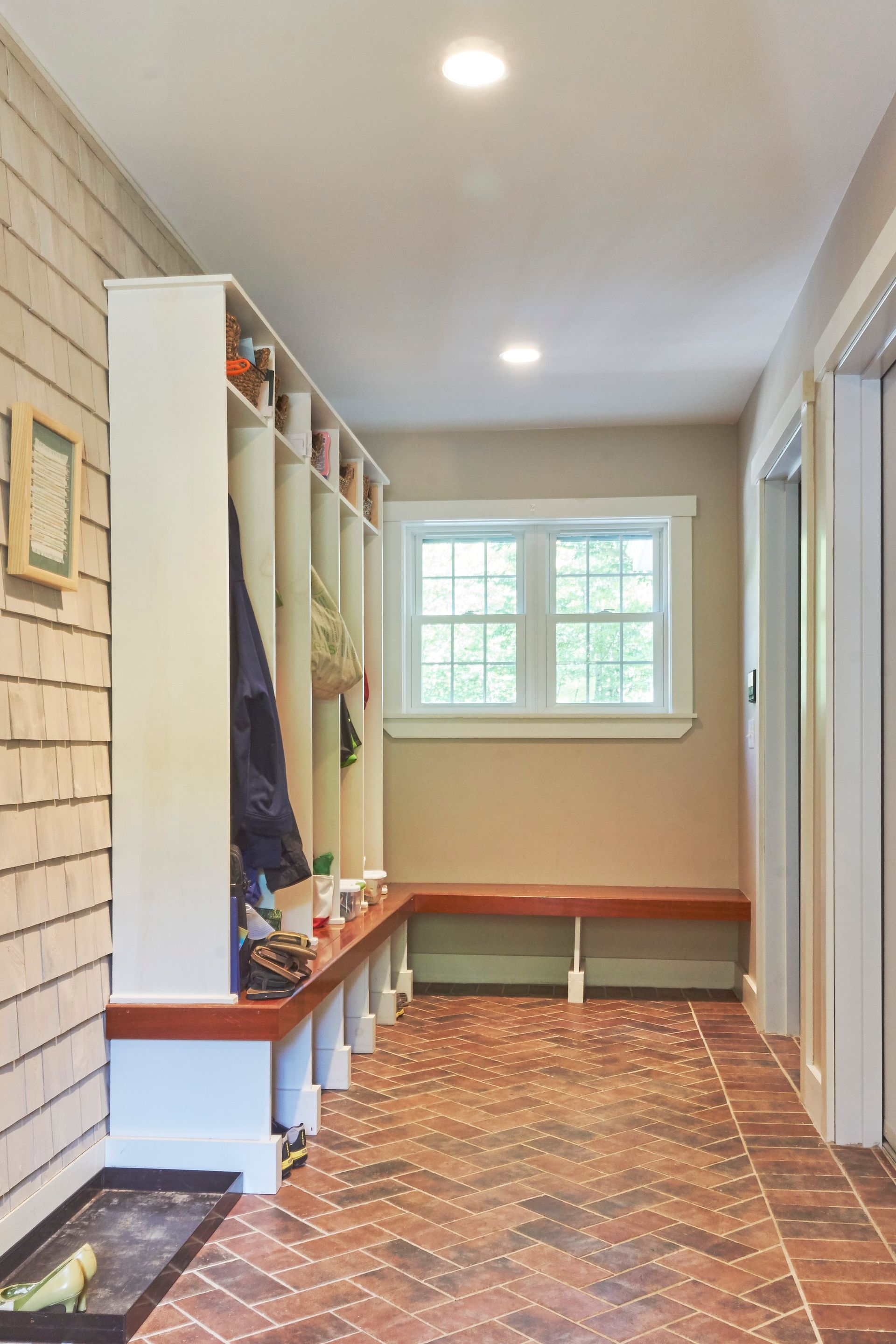 A hallway with a brick floor , a bench , and a window.