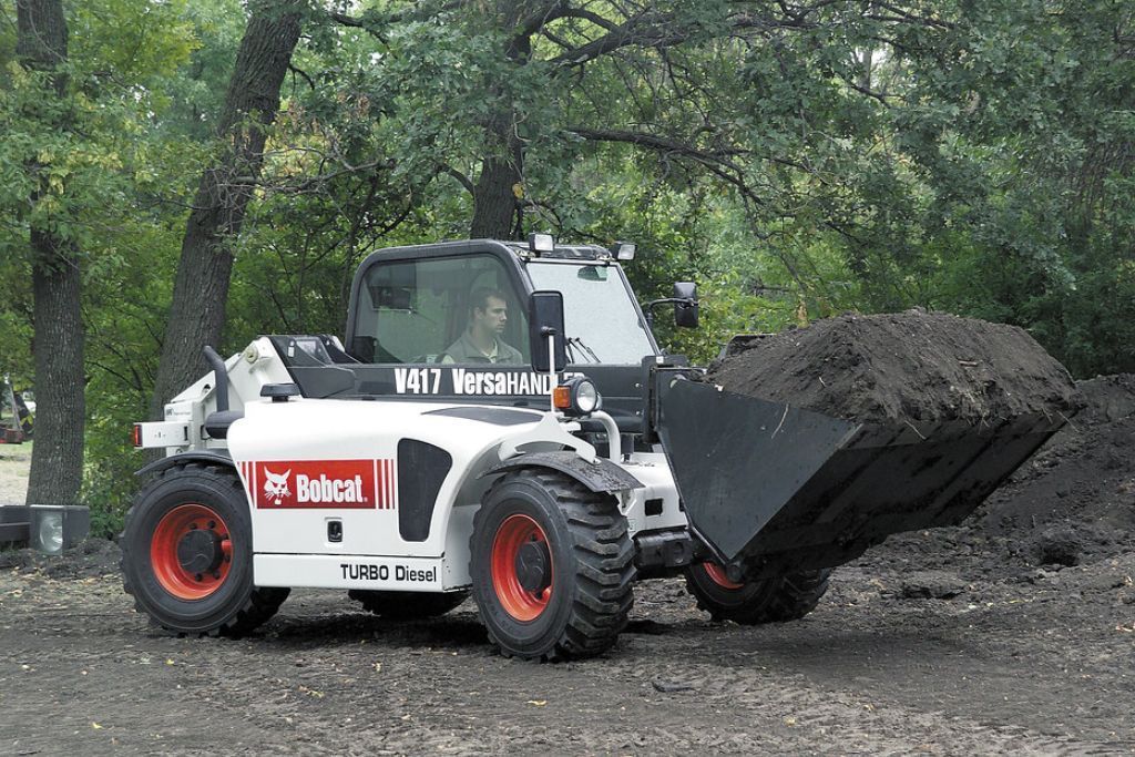 A bobcat tractor is carrying a large pile of dirt.