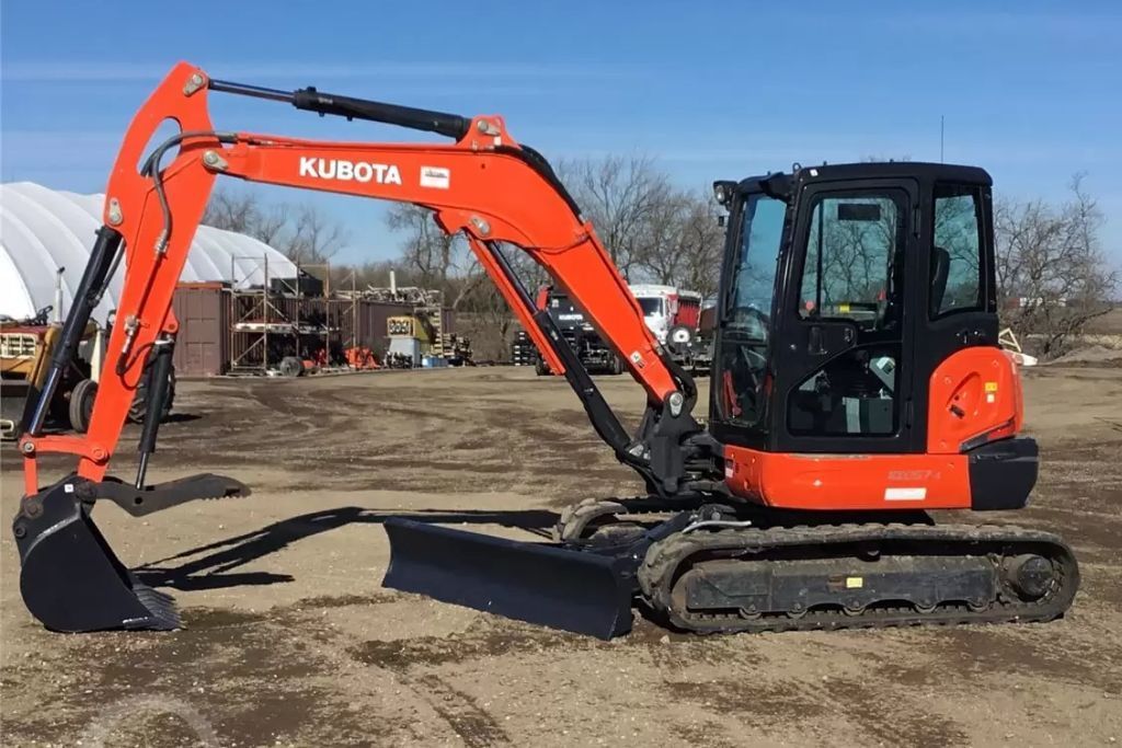 An orange backhoe is clearing the land and doing dirt work in preparation for home construction.
