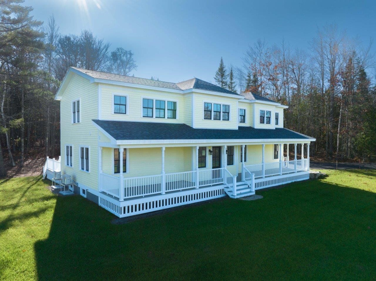 A large yellow house with a large porch is sitting on top of a lush green field.