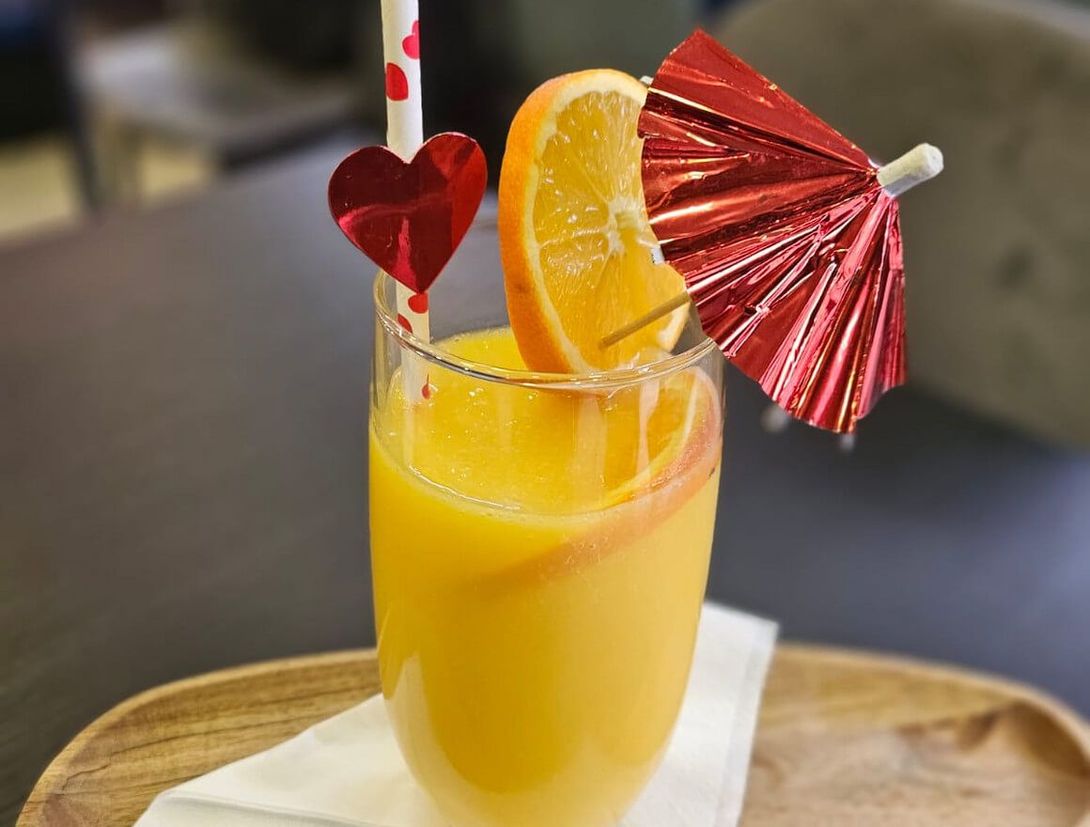 a glass of orange juice with a heart shaped straw and a red umbrella